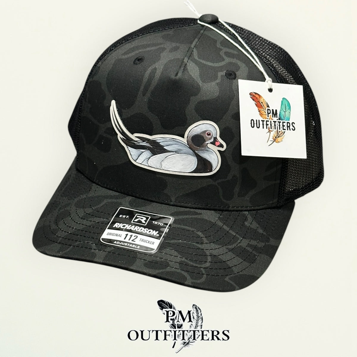 Hand-painted Long-Tailed Duck trucker hat displayed with PM Outfitters branded hang tag