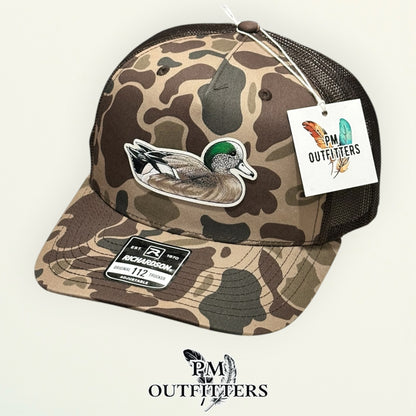 Hand-painted American Wigeon trucker hat displayed with PM Outfitters branded hang tag