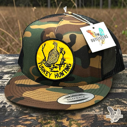 Turkey Hunting embroidered patch on a woodland camo and black Yupoong 6006 trucker hat, PM Outfitters