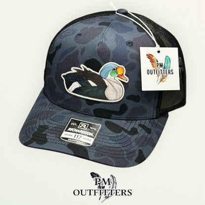 Hand-painted King Eider trucker hat displayed with PM Outfitters branded hang tag