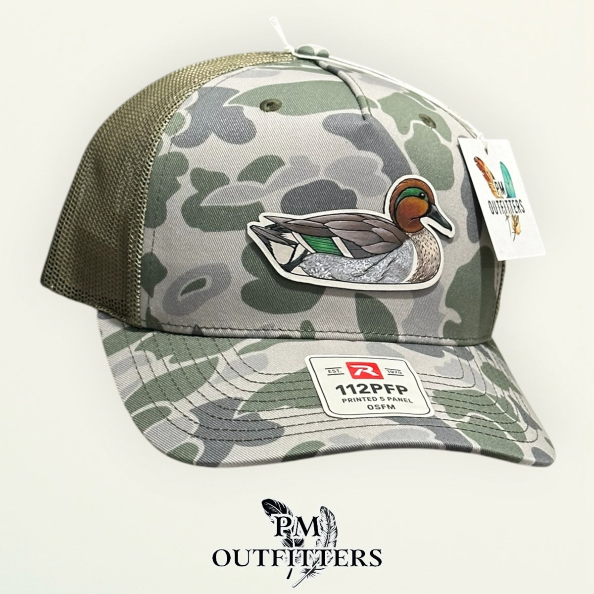 Marsh duck camo Richardson 112PFP trucker hat with hand-painted Green-Winged Teal patch, angled view, PM Outfitters True Originals