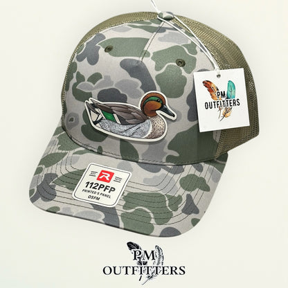 Hand-painted Green-Winged Teal trucker hat displayed with PM Outfitters branded hang tag