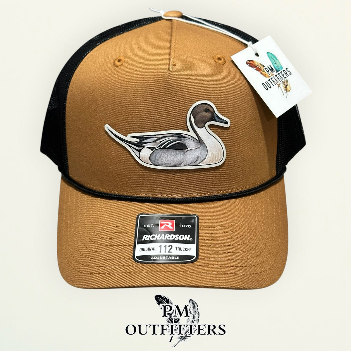 Side view of the hand-painted Northern Pintail patch on the caramel and black trucker hat, PM Outfitters True Originals