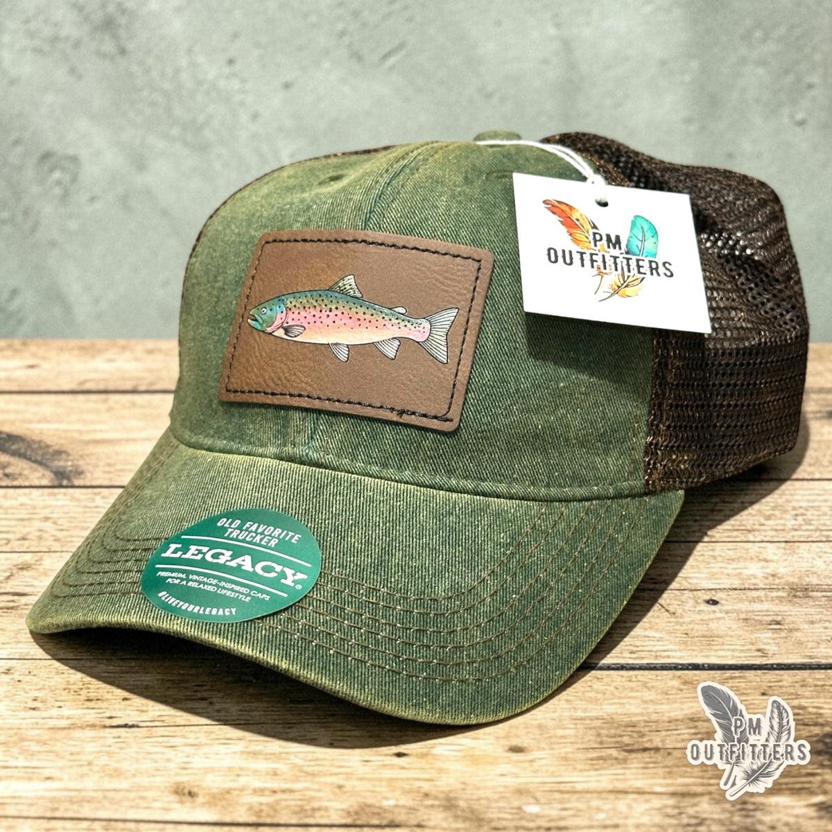 Hand-painted rainbow trout patch on an olive Legacy Old Favorite trucker hat with bronze mesh back, PM Outfitters True Originals