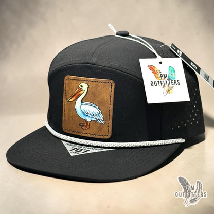 Hand-painted white pelican patch on an all-black Kamel 707 performance rope cap, PM Outfitters True Originals