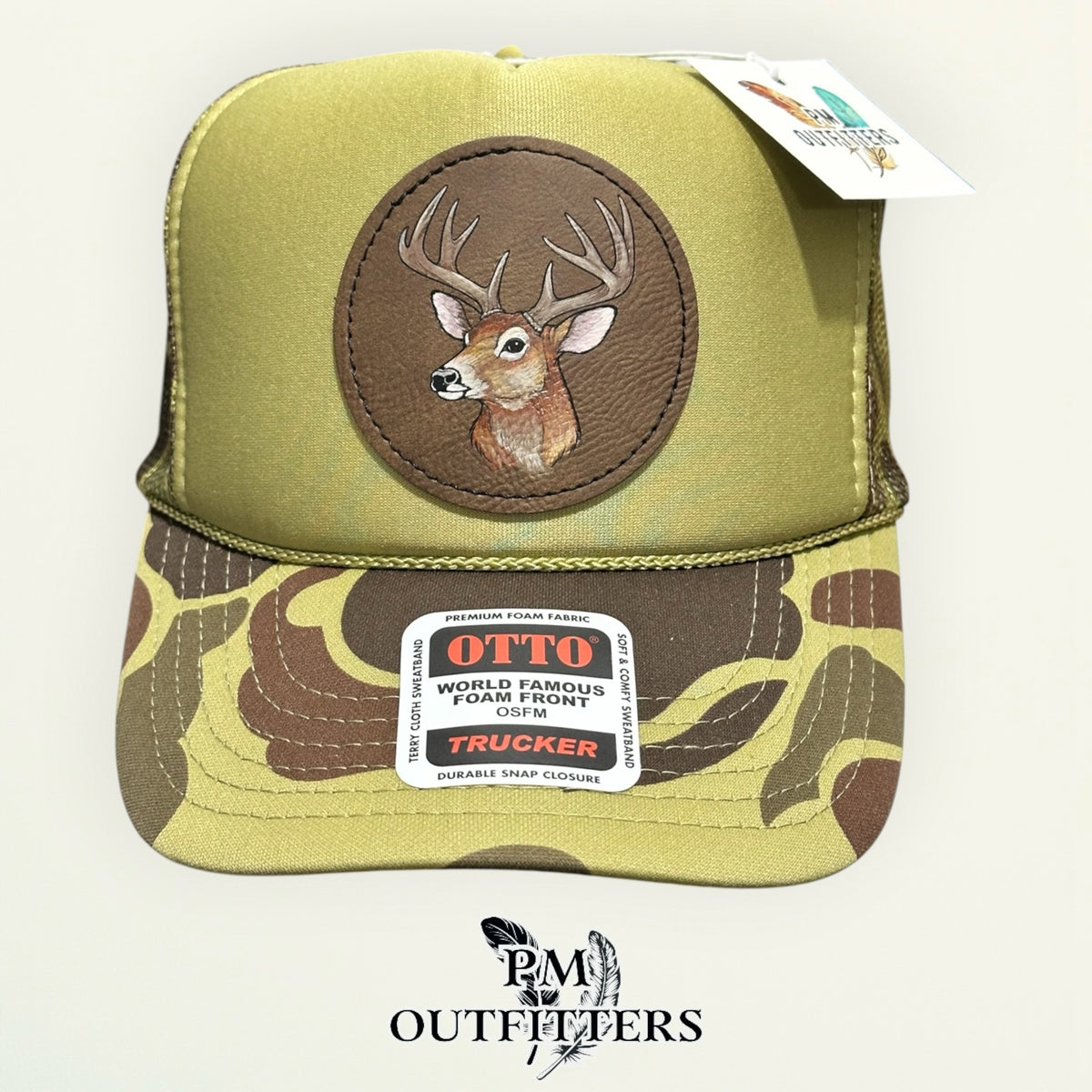 Hand-painted whitetail buck trucker hat displayed with PM Outfitters branded hang tag