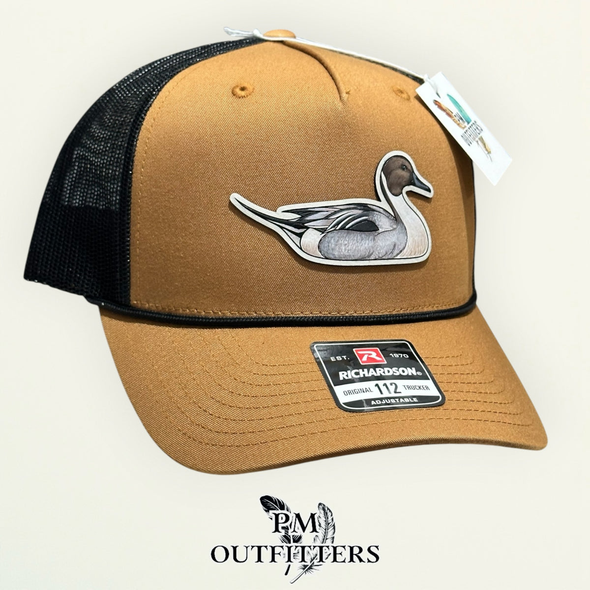 Caramel and black Richardson 112 trucker hat with hand-painted Northern Pintail patch, angled view, PM Outfitters True Originals